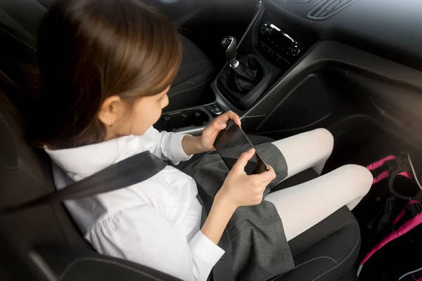 Schoolgirl using smartphone while going to school by car — Stock Photo, Image