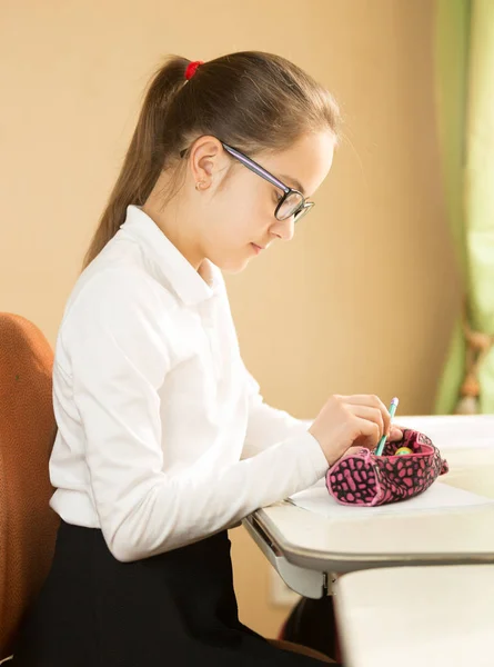 Schulmädchen sitzt hinter Tisch und nimmt Bleistift aus Bleistift — Stockfoto