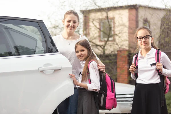 Mutlu anne ve iki kız okul çantaları arabaya poz ile — Stok fotoğraf