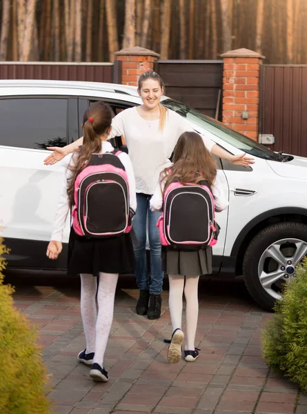 Happy young mother meeting her two daughters after school at car