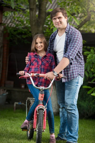 Smiling girl learning how to ride a bicycle with her father at p — Stock Photo, Image