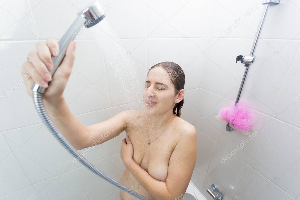 Brunette woman covering with hand and relaxing under shower