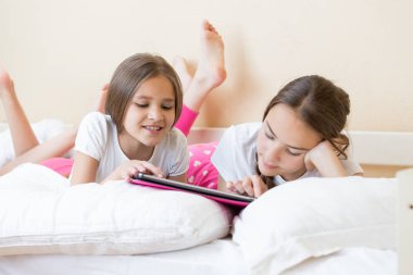 İki gülümseyen kız yatakta yatarken ve internet üzerinde dijital tarama 
