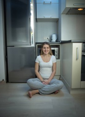 Kadın açık refrig yanında mutfak katında oturan pijama
