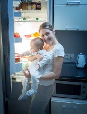Gülümseyen kadın mutfak üzerinde bebek oğluyla geceleri ayakta