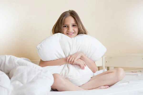 Vacker brunett flicka sitter på sängen och kramas vit kudde — Stockfoto