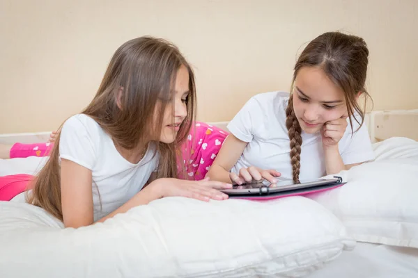 Dwie piękne dziewczyny w piżamie leży i za pomocą cyfrowego tabletu — Zdjęcie stockowe