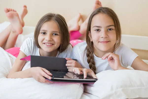 Two smiling girls lying in bed and using digital tablet — Stock Photo, Image