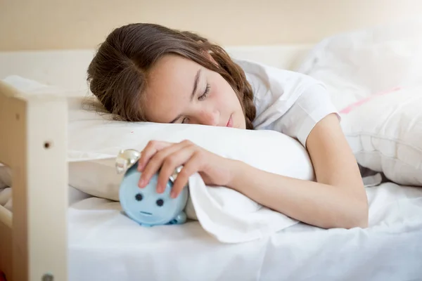 Cute teenage girl holding alarm clock under pillow — Stock Photo, Image