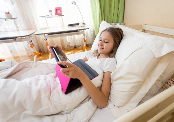 Улыбающаяся девочка-подросток с помощью цифрового планшета в постели — стоковое фото
