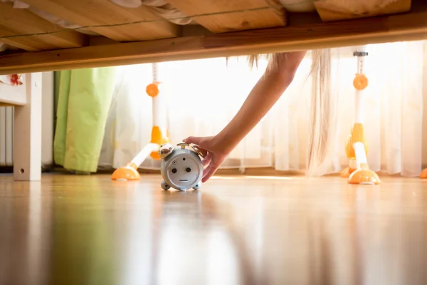 目覚まし時計のベッドの下に達する女性の手 — ストック写真