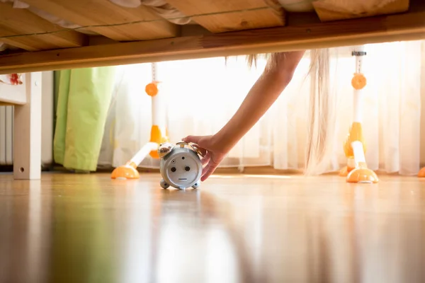 Kvinnlig hand når under sängen för väckarklocka — Stockfoto