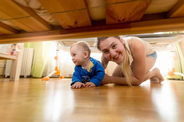 Счастливая мать с маленьким мальчиком ищут под кроватью — стоковое фото