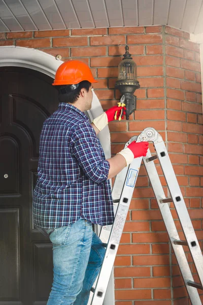 Junger Arbeiter repariert Outdoor-Lampe im Haus — Stockfoto
