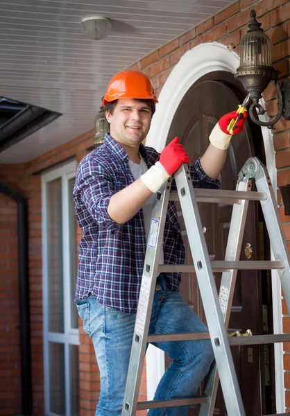 Hombre electricista en hardhat de pie escalera y reparación de la —  Fotos de Stock