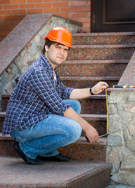 Smiling male worker measuring stone staircase with measuring tap — Stock Photo, Image