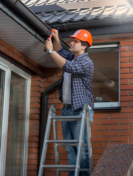 Arbeiter steht auf Leiter und repariert Dachrinne am Haus — Stockfoto