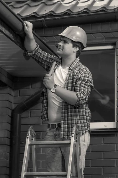Черно-белое фото рабочего, ремонтирующего крышу и водосток — стоковое фото