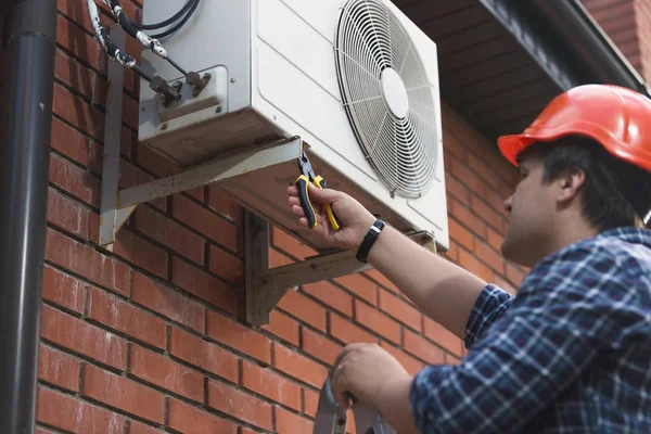 Technicus in veiligheidshelm buiten airconditioning-installatie aansluiten — Stockfoto