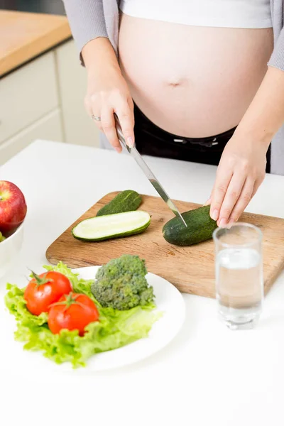 Фотография беременной женщины, делающей овощной салат на кухне — стоковое фото