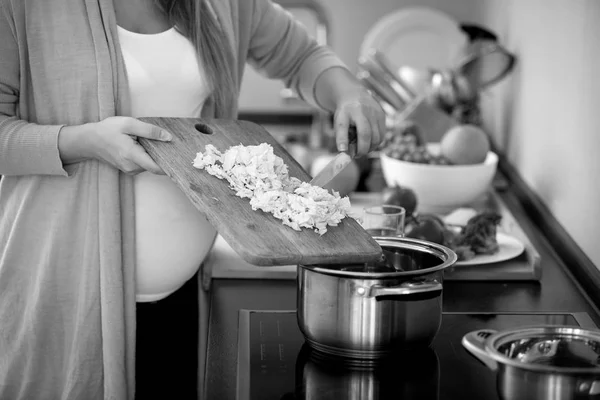 Closeup black and white photo of pregnant woman cooking vegetabl