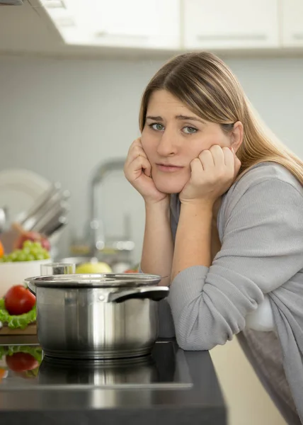 Retrato de mujer triste apoyada en la mesa en la cocina mientras cocina —  Fotos de Stock