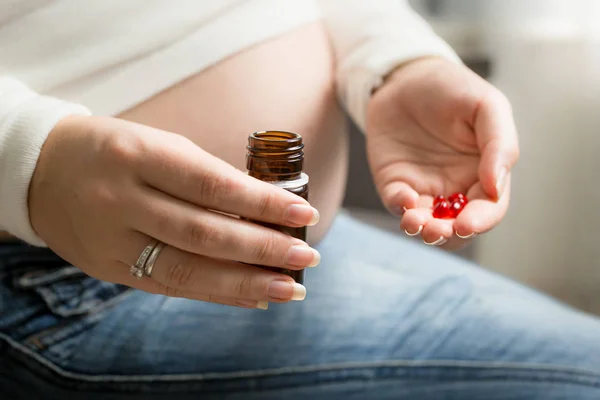 Крупним планом фото вагітної жінки, що тримає червону таблетку на руці — стокове фото