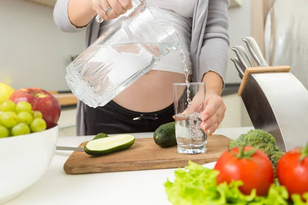 Primer plano de la mujer vertiendo agua en vidrio en la cocina —  Fotos de Stock