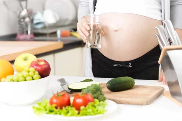 Unga gravid kvinna som håller glas vatten på kök — Stockfoto