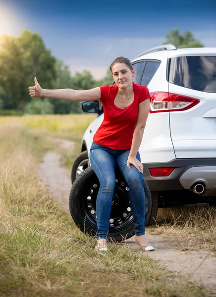 Грустная женщина сидит на колесе на сломанной машине в подал и автостопом — стоковое фото
