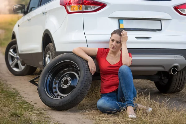 タイヤがパンクで車の横に座って、ヘルを待っている女 — ストック写真