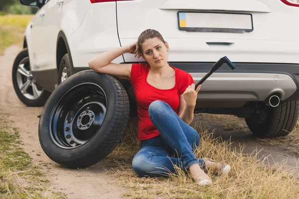 若い女性の壊れた車で地面に座ってホイール wr を保持 — ストック写真