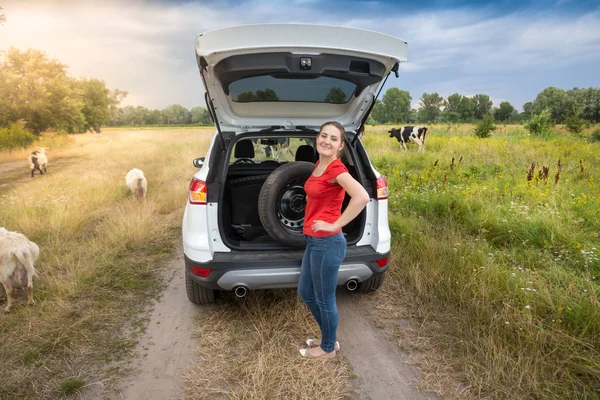 Junge Frau posiert mit Reserverad an kaputtem Auto auf dem Land — Stockfoto