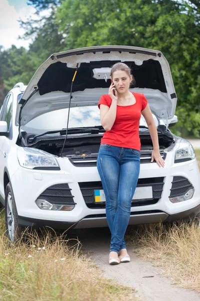 Beautiful young woman leaning on broken car and calling auto ser — Stock Photo, Image