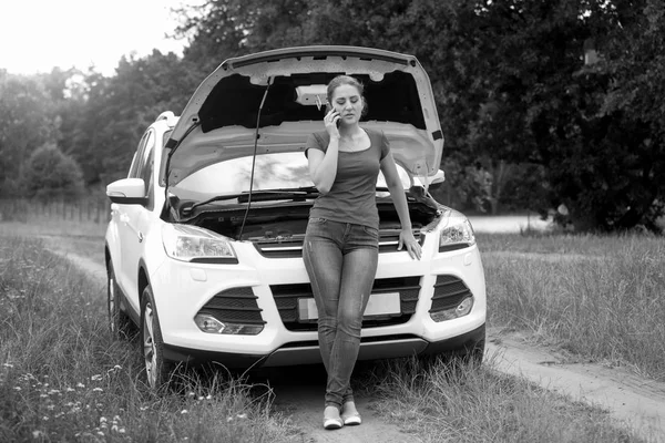Immagine in bianco e nero di giovane donna in piedi in auto rotta e — Foto Stock