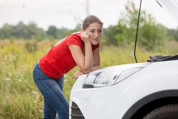 Young woman looking at broken car motor on rural road — Stock Photo, Image