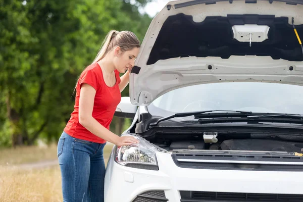 Portrait of upset woman looking under the bonnet of overheated c — Stock Photo, Image