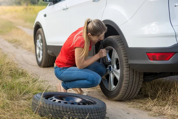Young woman changing flat tire in field — Stock Photo, Image