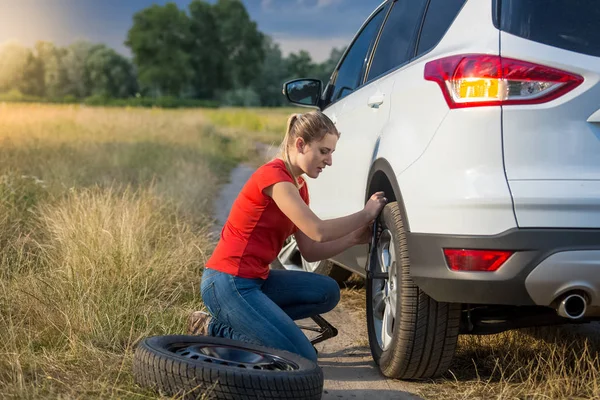 Mujer joven cambiando neumático pinchado en el camino rural — Foto de Stock