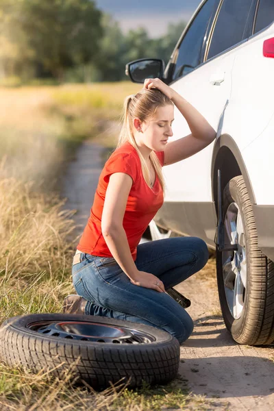 Mujer sentada en el coche roto y tratando de cambiar el neumático pinchado —  Fotos de Stock