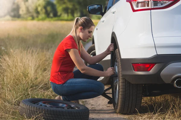 Young woman changing flat tire in field — Stock Photo, Image