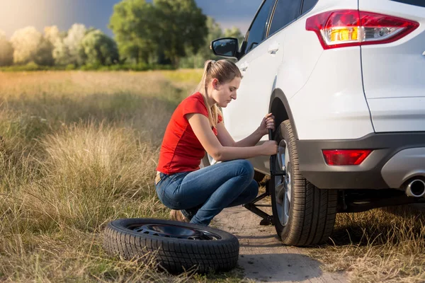 Beautiful woman changing flat tire in field — Stock Photo, Image