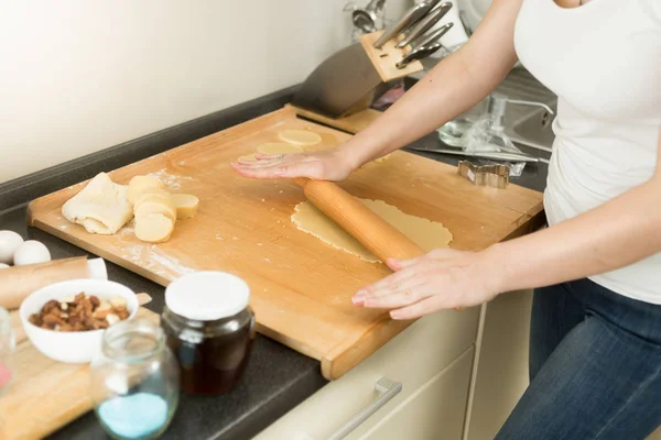 Nahaufnahme einer jungen Frau, die Teig mit Nadel auf Holzbrett rollt — Stockfoto