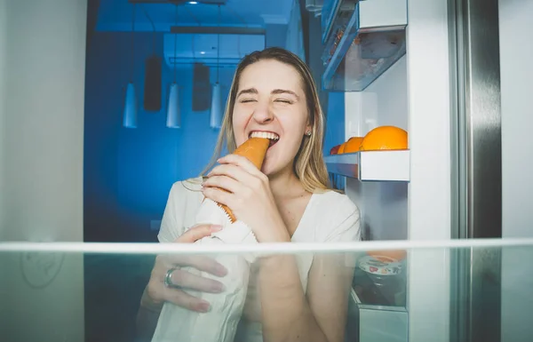 Portrait of young hungry woman eating bread at night — Stock Photo, Image