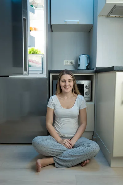 Donna sorridente in pigiama seduta sul pavimento in cucina accanto a ope — Foto Stock