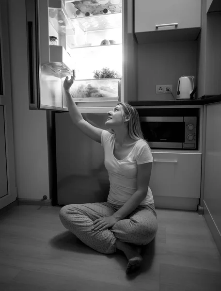 Černobílý obraz mladé ženy sedí na podlaze a reachi — Stock fotografie