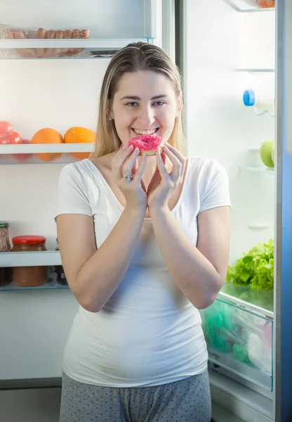 Porträtt av kvinna äta stora donut på kök på natten — Stockfoto