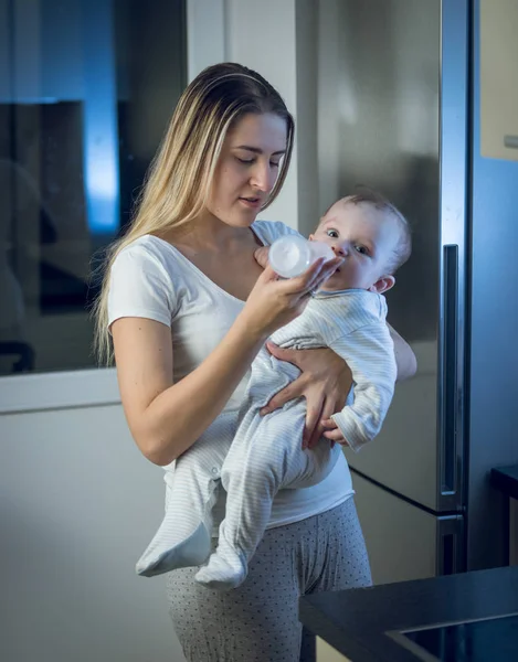 Retrato de la madre dando leche del biberón a su bebé por la noche — Foto de Stock