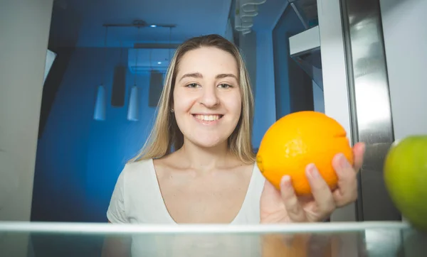 Улыбающаяся женщина, держащая апельсин и заглядывающая внутрь — стоковое фото