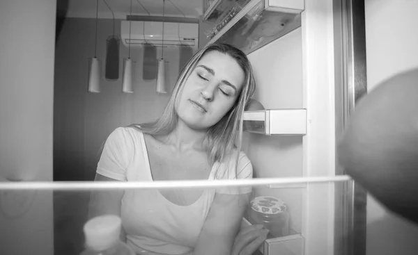 Retrato preto e branco de mulher sonolenta apoiada na geladeira — Fotografia de Stock